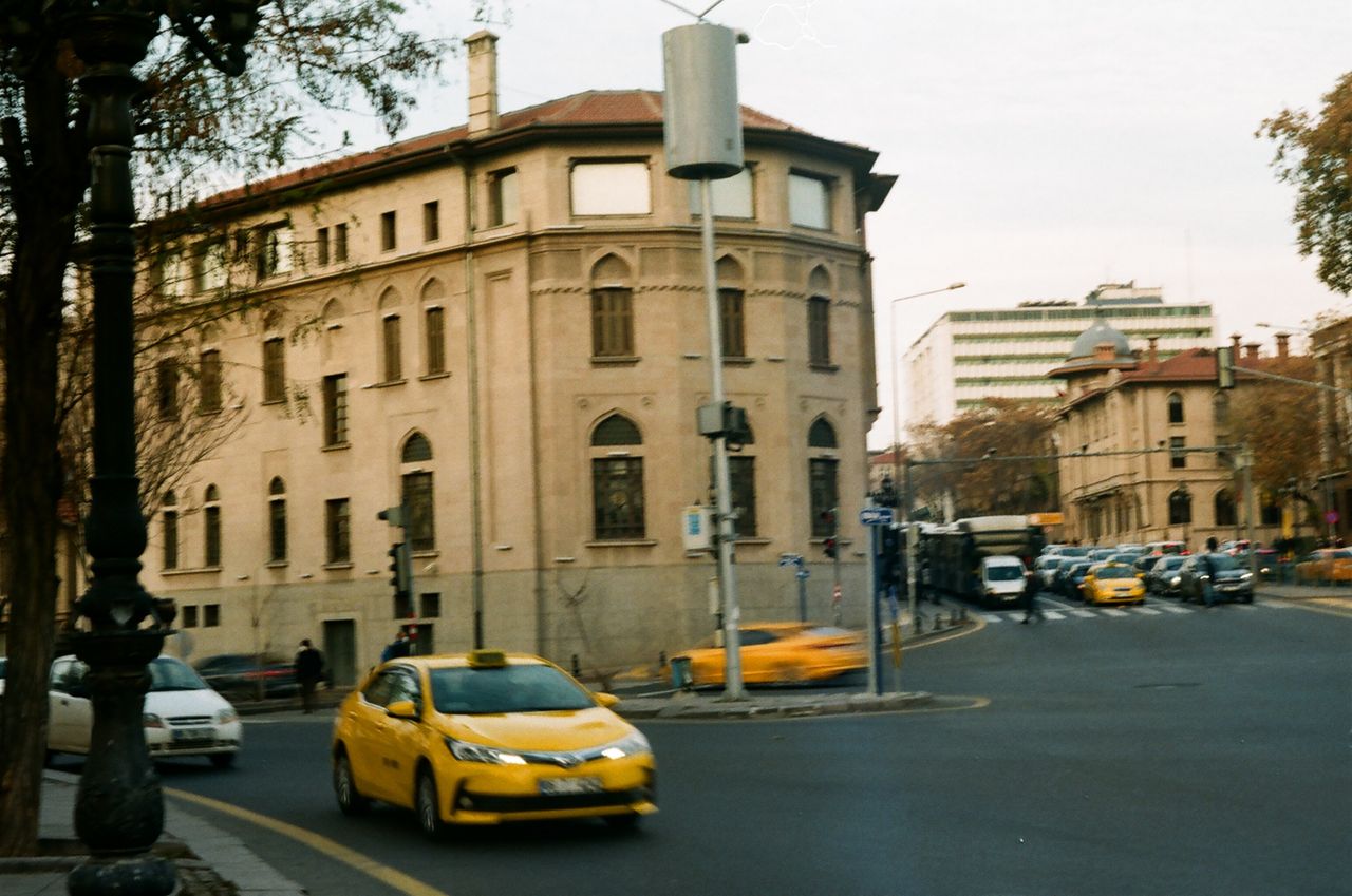 about-img Bustling urban street corner with taxis and historical buildings in Ankara, Türkiye.