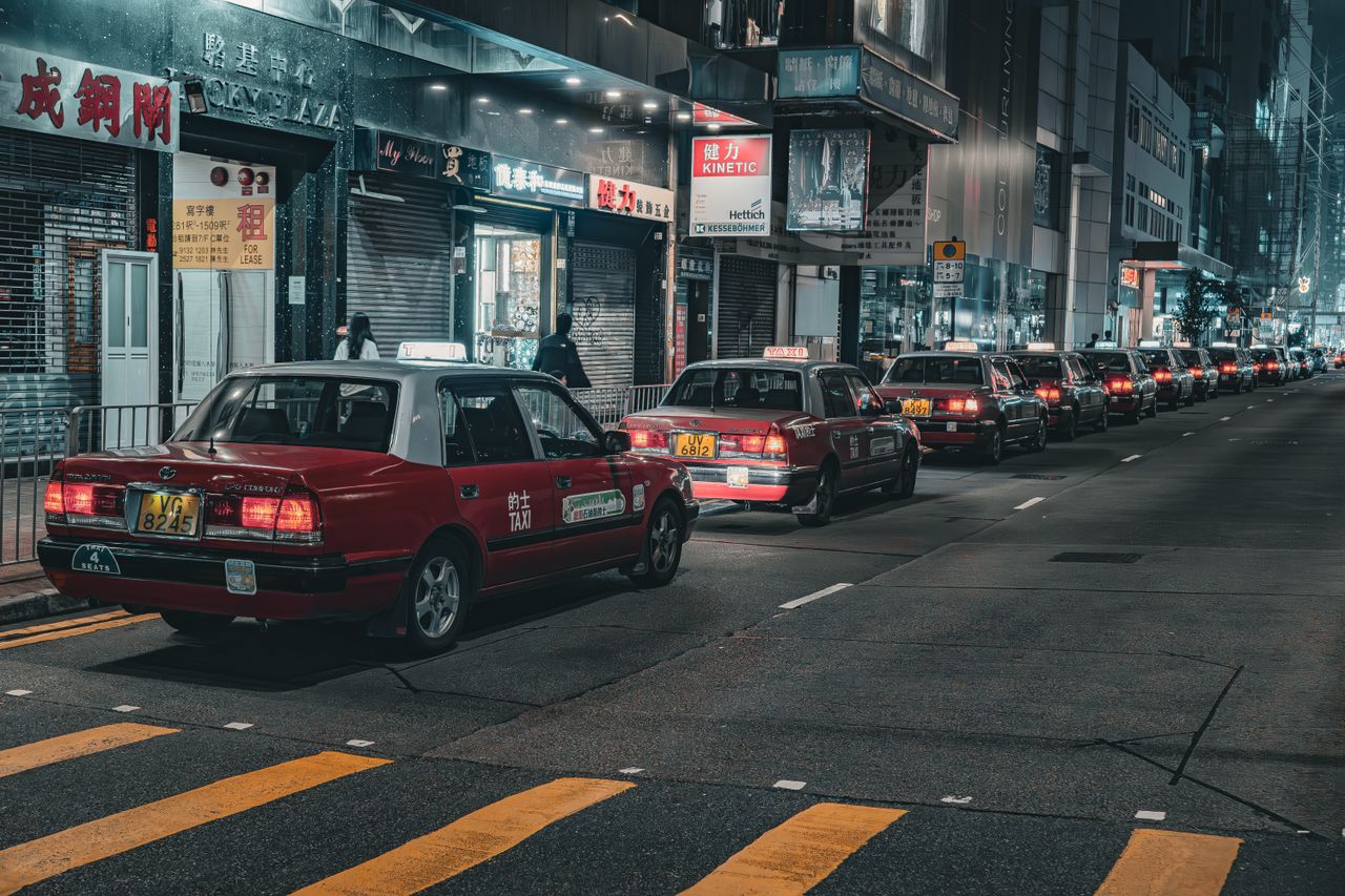about-01 A street in Hong Kong bustling with red taxis at night, capturing urban life and city lights.