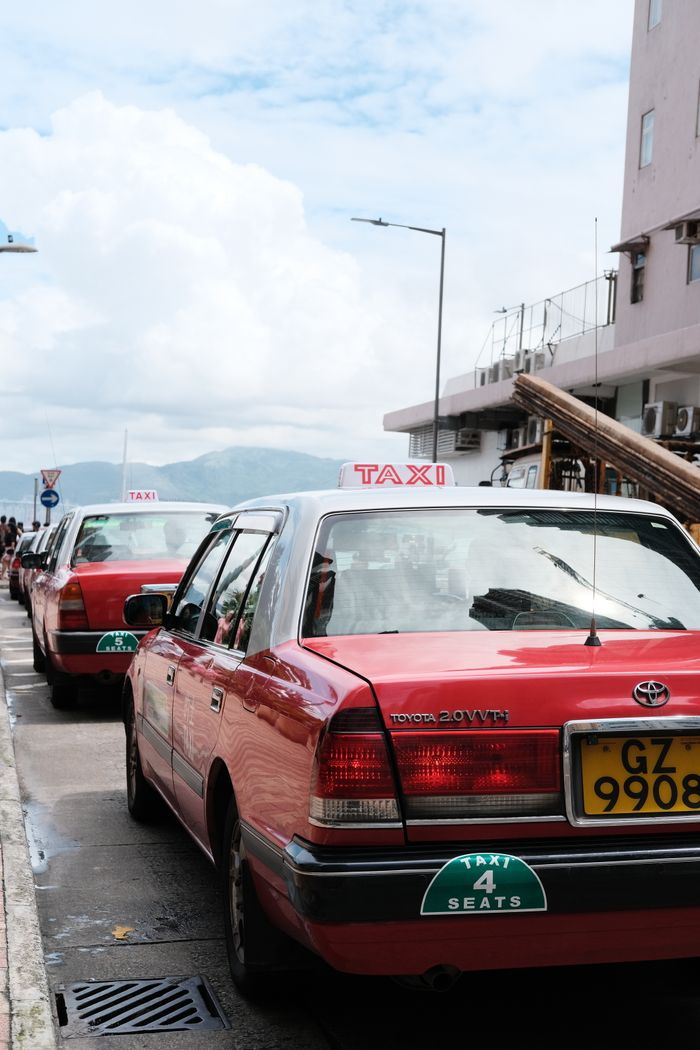services-04 Red taxis parked along a street in a city with a clear sunny sky, ready for passengers.